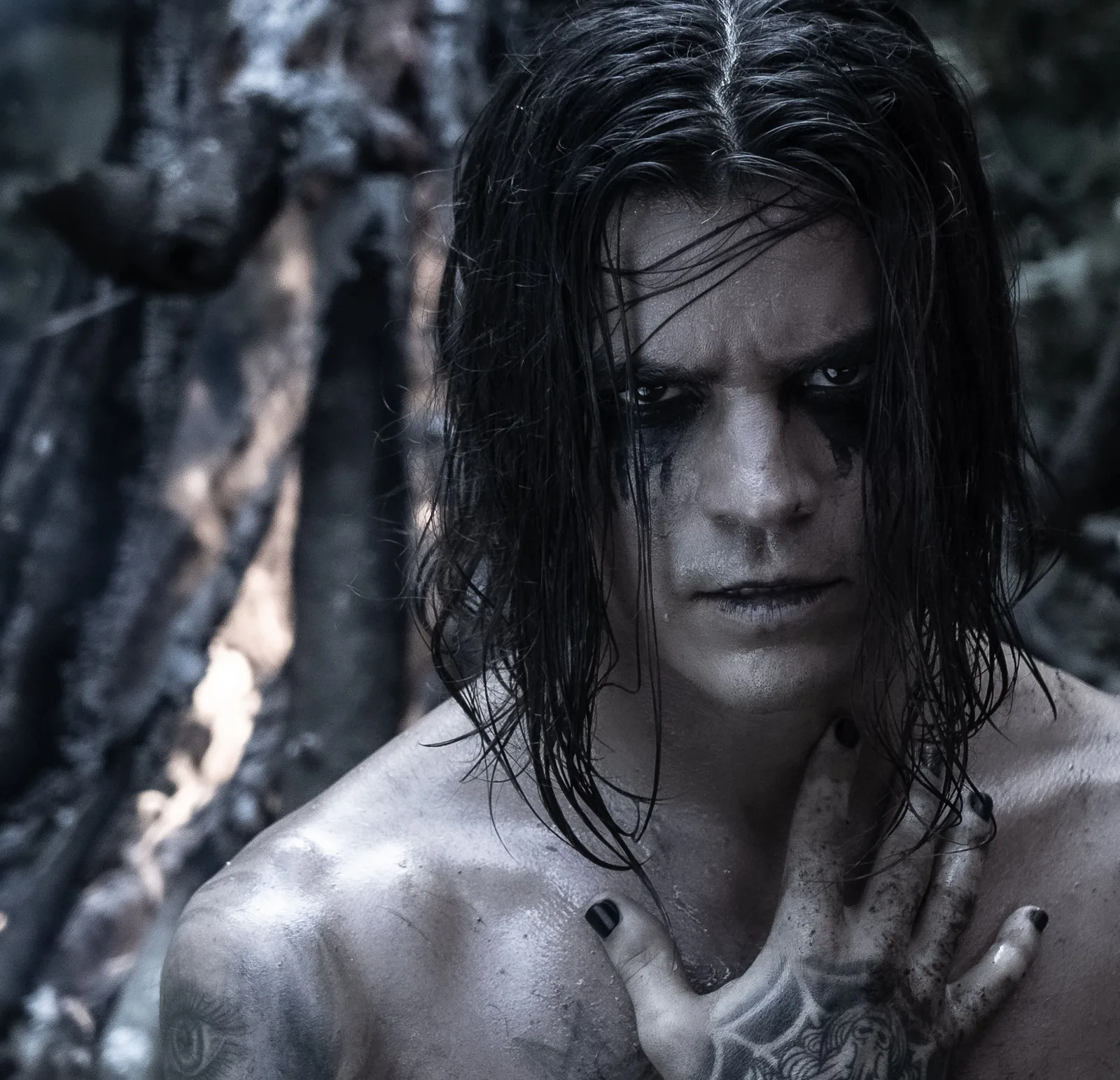 Close in the burnt forest: black-rimmed eyes with makeup running down both cheeks, wet hair parted at the centre.
