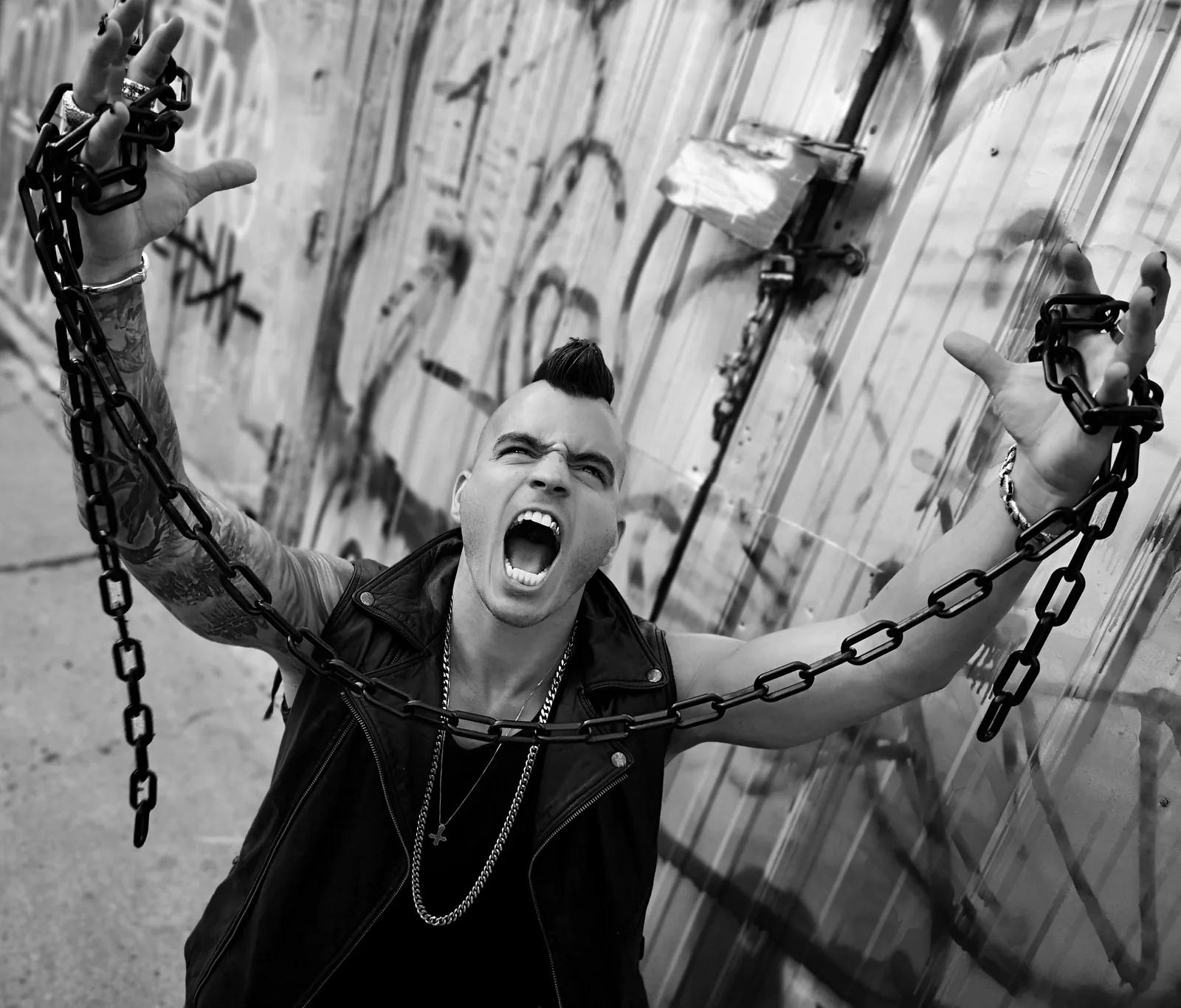 Mohawk up, chains stretched from both fists, Daemon Grey screams skyward in front of a graffiti-covered wall.