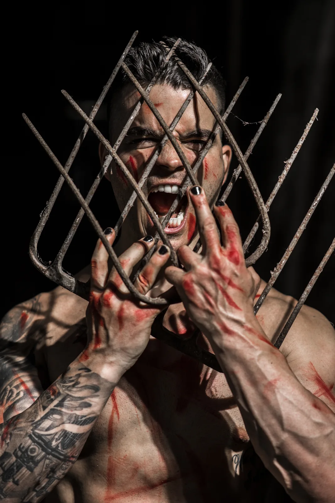 Daemon Grey screams through the crossed tines of a rusted pitchfork, red streaks over his hands and chest.